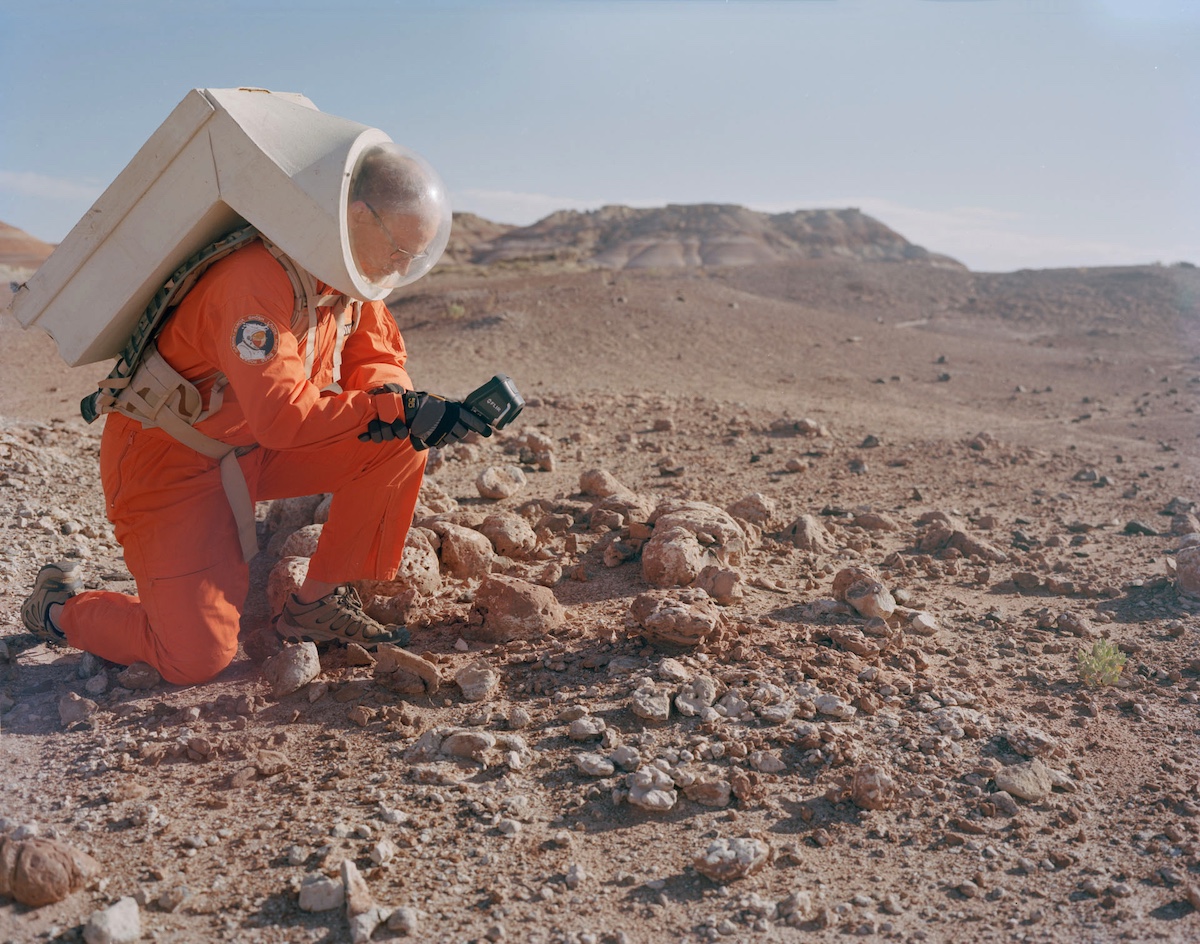 Photograph of an analog astronaut in a simulated spacesuit conducting geological field work in the Utah desert terrain surrounding MDRS