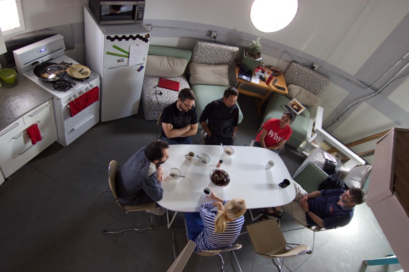 Interior photograph of the MDRS habitat upper deck showing crew members at work stations and the shared kitchen area